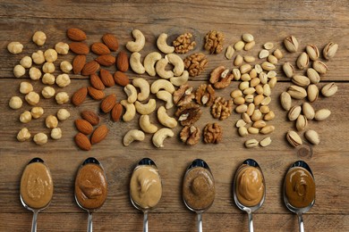 Photo of Tasty nut butters in spoons and raw nuts on wooden table, flat lay