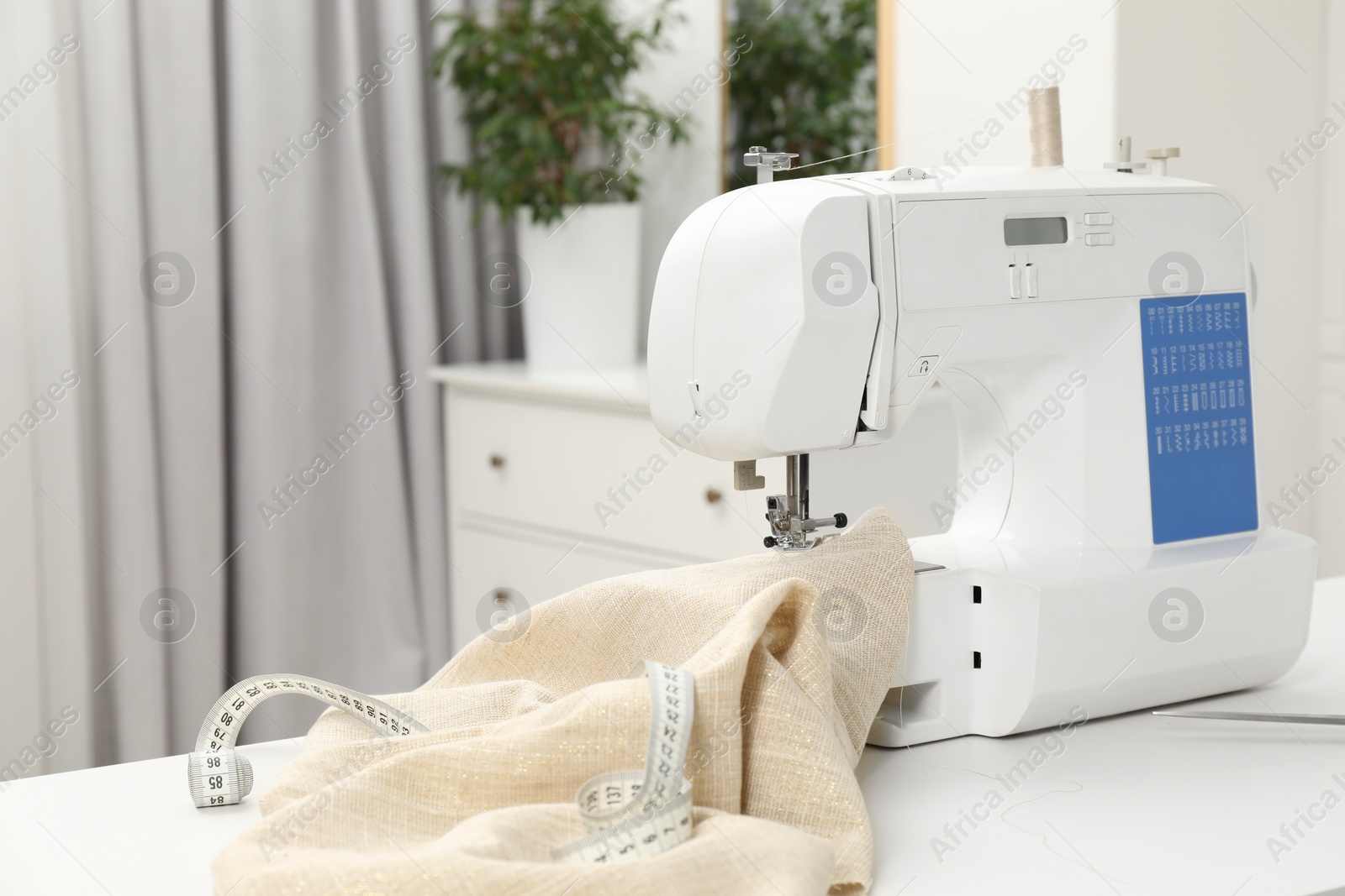 Photo of Sewing machine, measuring tape and fabric on white table in workshop