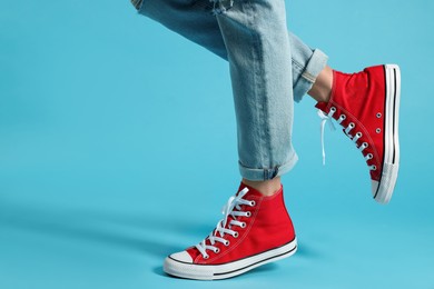 Woman in stylish gumshoes on light blue background, closeup. Space for text