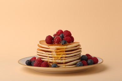 Photo of Stack of tasty pancakes with raspberries, blueberries and honey on pale orange background