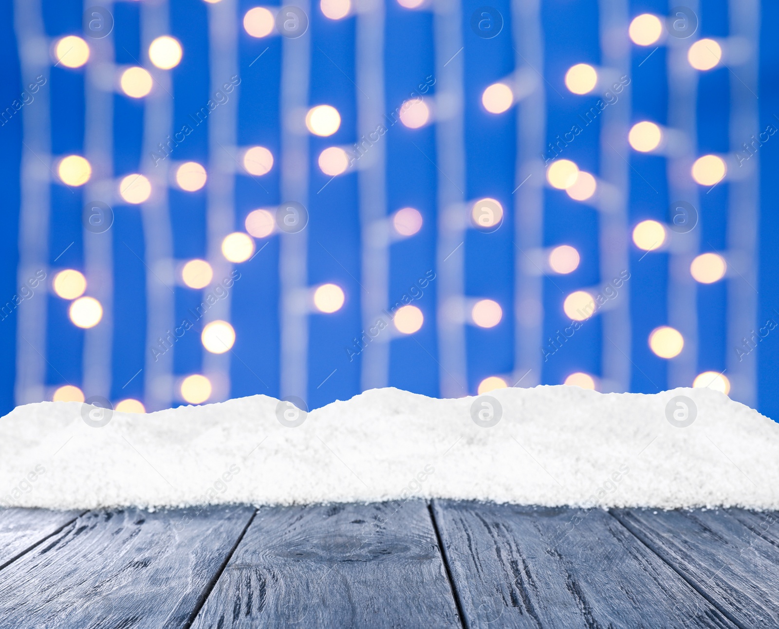 Image of Wooden surface with heap of snow and blurred Christmas lights on background, bokeh effect 