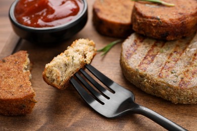 Photo of Fork with piecedelicious vegan cutlet on wooden table, closeup