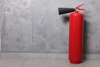 Red fire extinguisher near grey wall, space for text