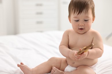 Cute baby boy with wooden rattle on bed at home. Space for text