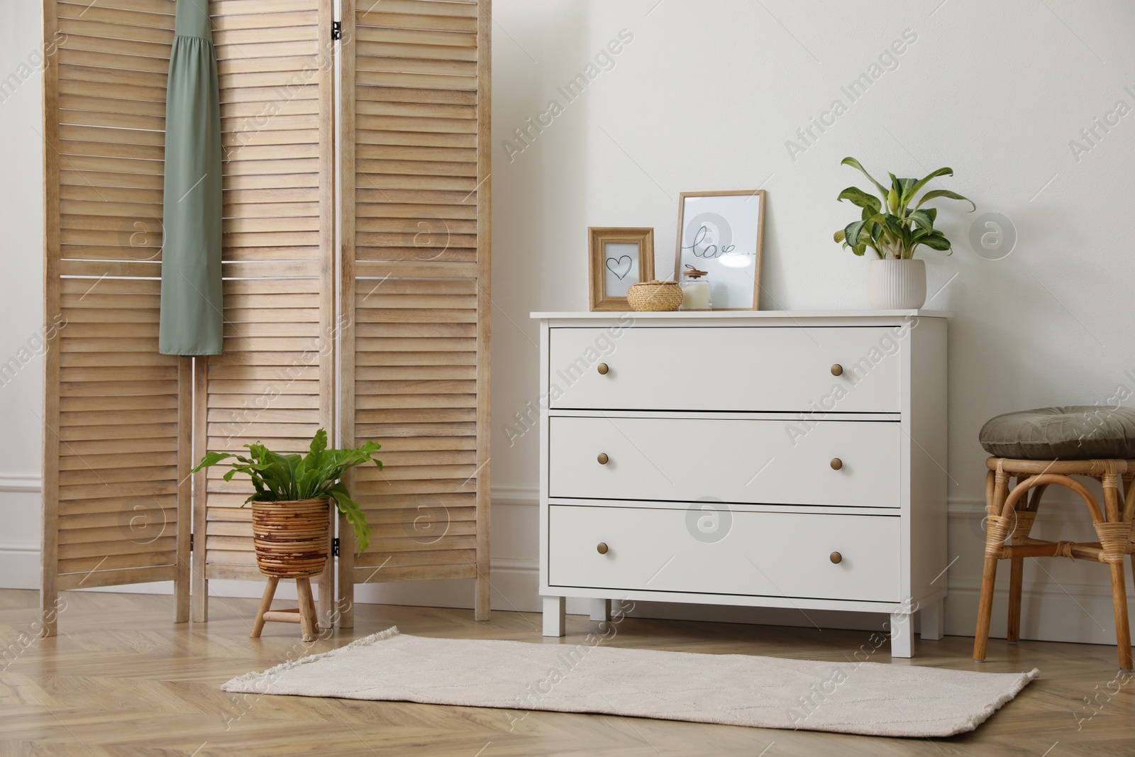 Photo of Stylish room with wooden folding screen and chest of drawers near white wall. Interior design