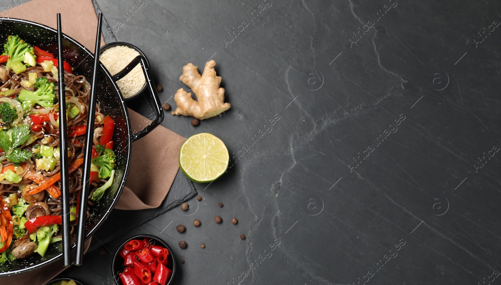 Photo of Wok with noodles, mushrooms, vegetables and other products on black table, flat lay. Space for text