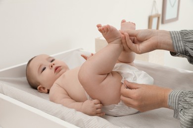 Mother changing baby's diaper at home, focus on hands