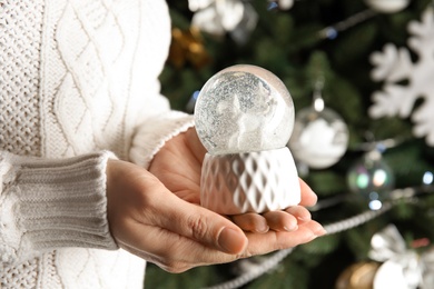 Photo of Woman holding snow globe near Christmas tree, closeup