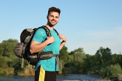 Young man with backpack and sleeping bag near lake. Space for text