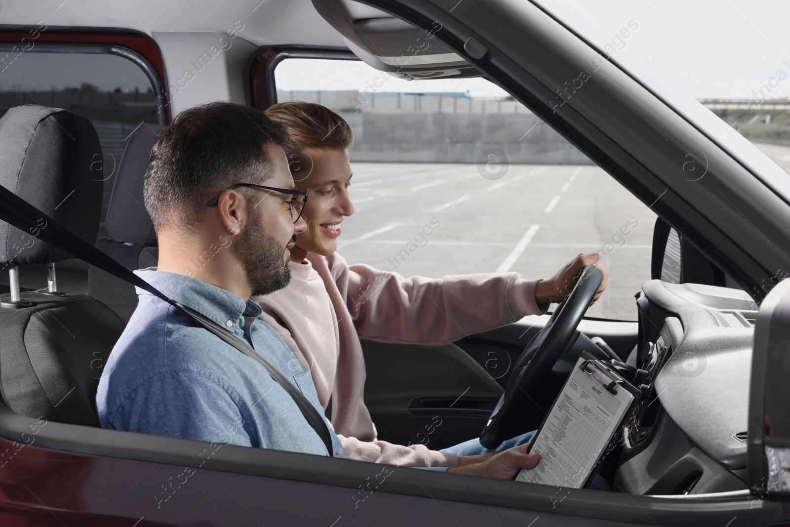 Photo of Driving school. Happy student passing driving test with examiner in car at parking lot