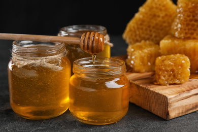 Photo of Honey dripping from dipper into jar on grey table