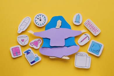 Woman paper figure with personal hygiene products on yellow background, flat lay