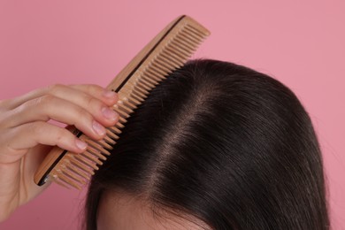 Photo of Woman with comb examining her hair and scalp on pink background, closeup