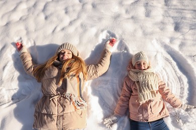Photo of Family time. Happy mother and her daughter making snow angels on sunny winter day, above view
