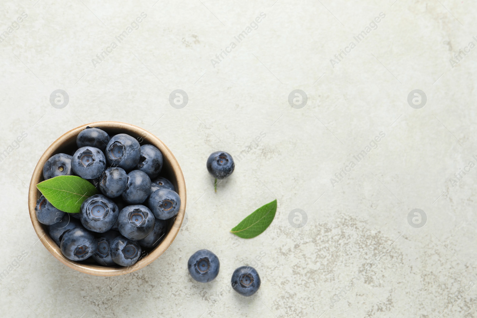 Photo of Tasty fresh blueberries in bowl on light table, flat lay. Space for text