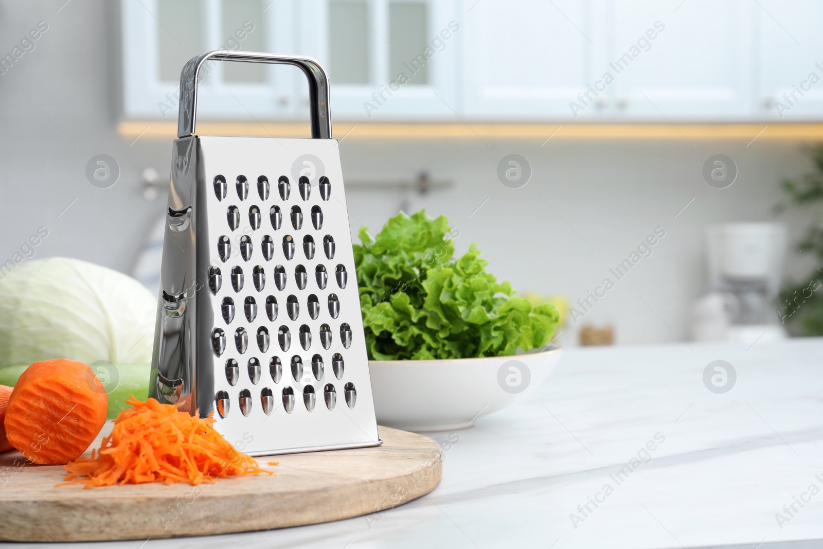 Photo of Grater and fresh ripe carrot on white table in kitchen. Space for text