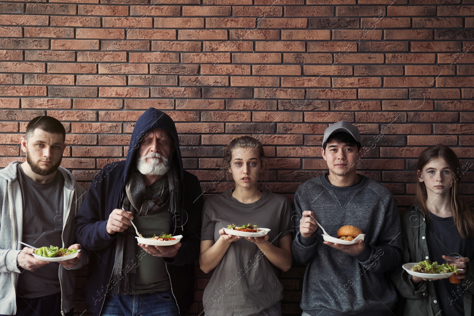 Photo of Poor people with plates of food at wall indoors