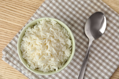 Photo of Bowl with tasty cooked rice on wooden table, flat lay