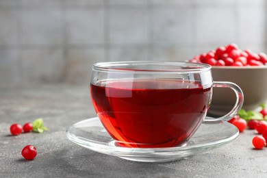 Photo of Tasty hot cranberry tea in glass cup and fresh berries on light grey textured table