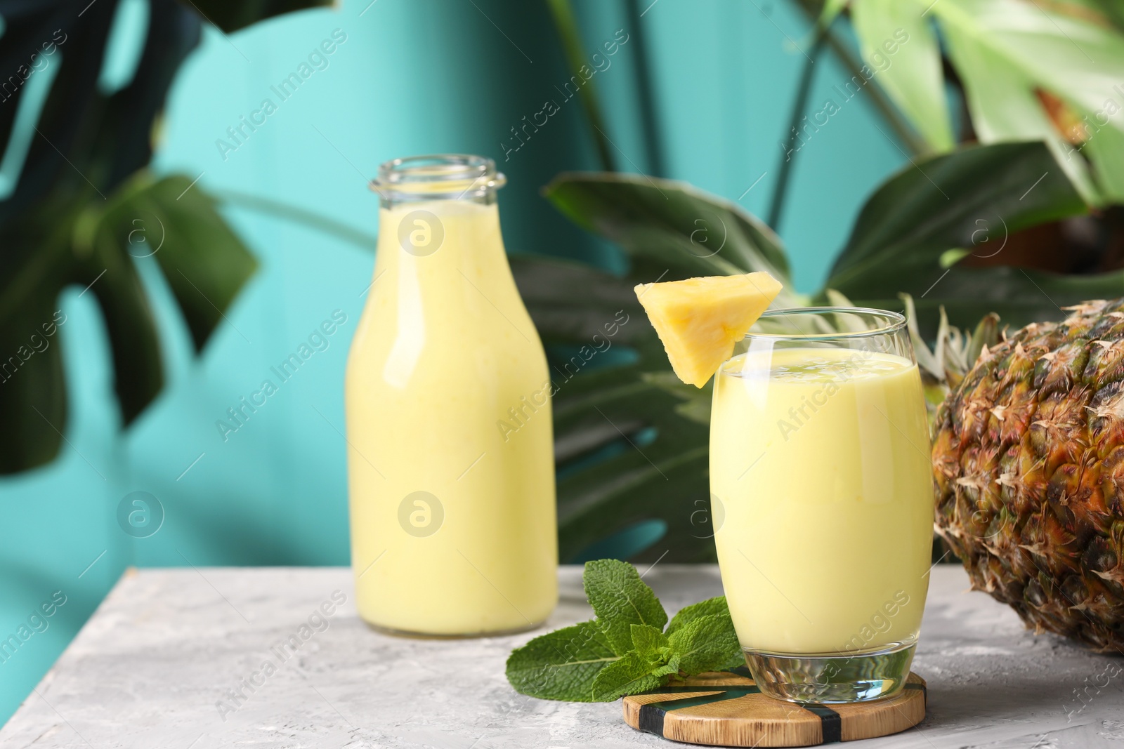 Photo of Tasty pineapple smoothie, mint and fruit on grey textured table. Space for text