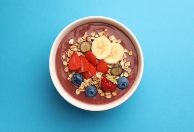 Photo of Delicious smoothie bowl with fresh berries, banana and granola on light blue background, top view