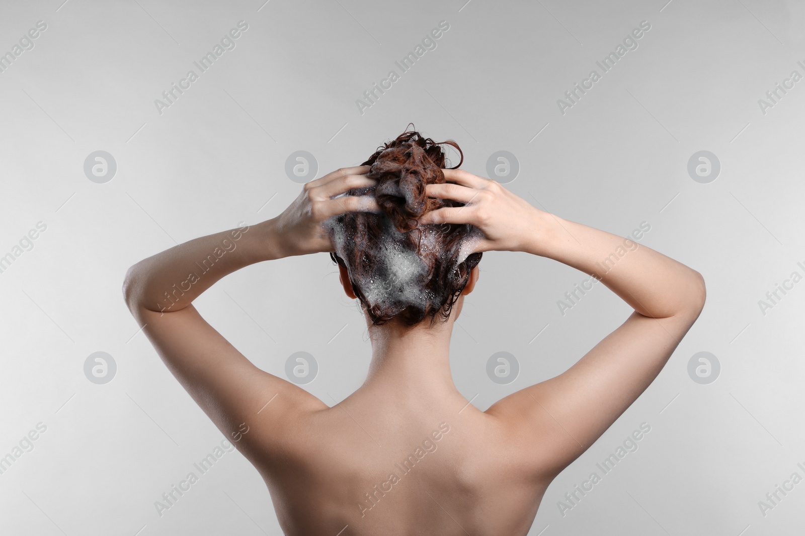 Photo of Young woman washing her hair with shampoo on light grey background, back view