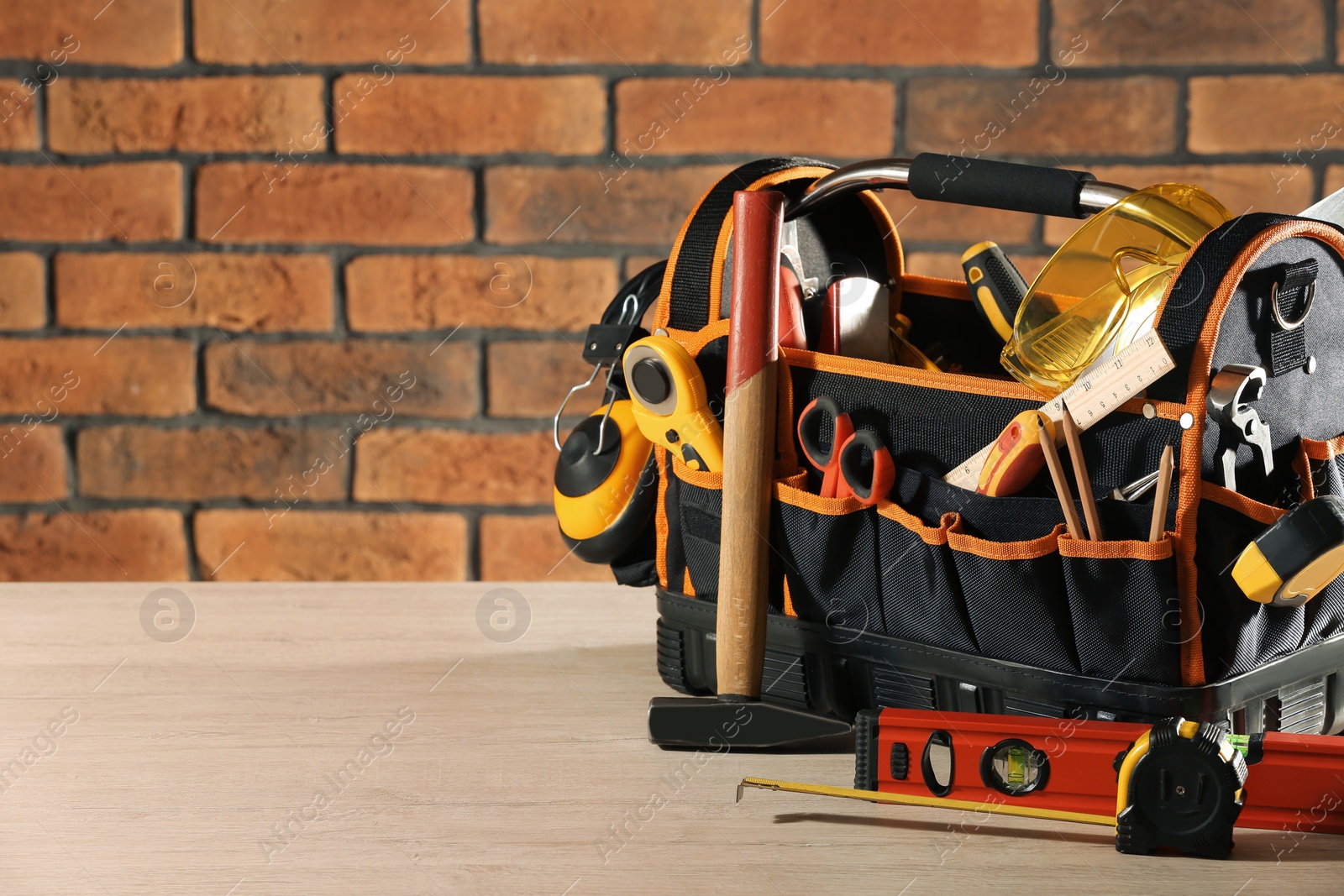 Photo of Bag with different tools for repair on white wooden table near brick wall. Space for text