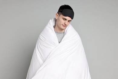 Photo of Man in pyjama and sleep mask wrapped in blanket on grey background