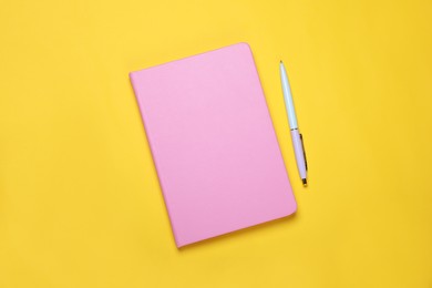 Photo of Closed pink notebook and pen on yellow background, flat lay