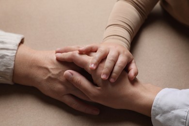 Photo of Family holding hands together on brown background, closeup