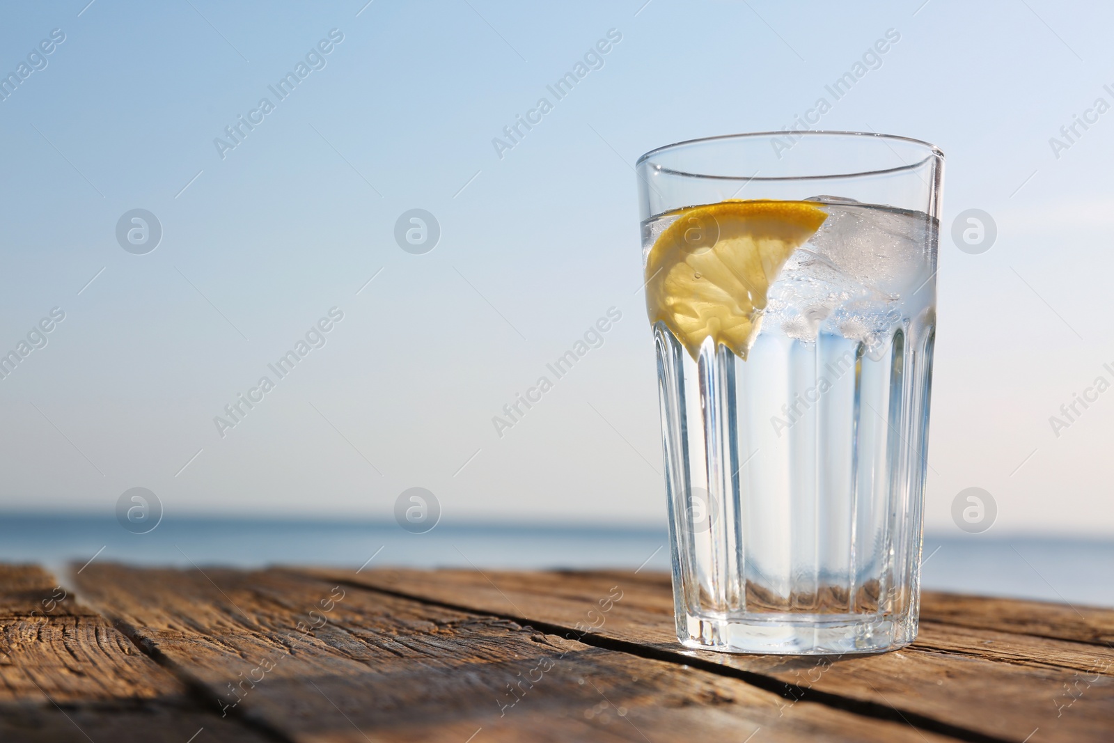 Photo of Wooden table with glass of refreshing lemon drink on hot summer day outdoors, space for text