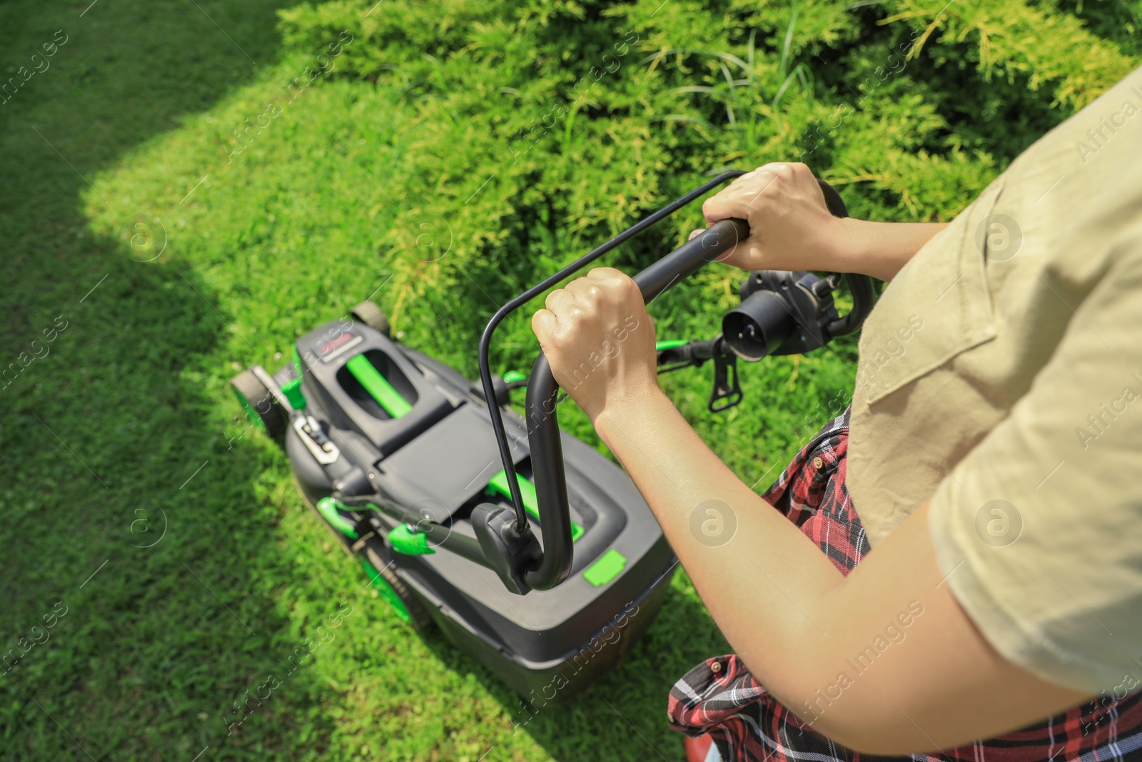 Photo of Woman cutting grass with lawn mower in garden on sunny day, closeup