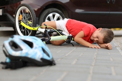 Photo of Little boy fallen from bicycle after car accident and helmet on road