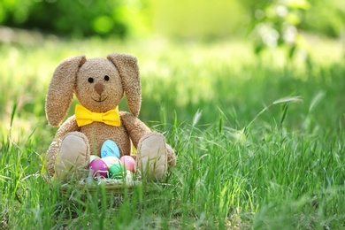 Photo of Toy bunny and basket with Easter eggs on grass