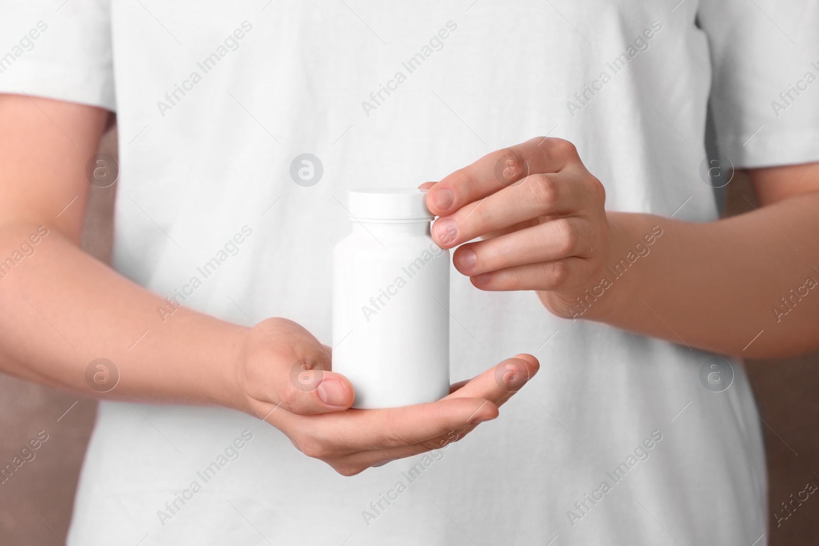 Photo of Woman holding blank white bottle with vitamin pills against light brown background, closeup