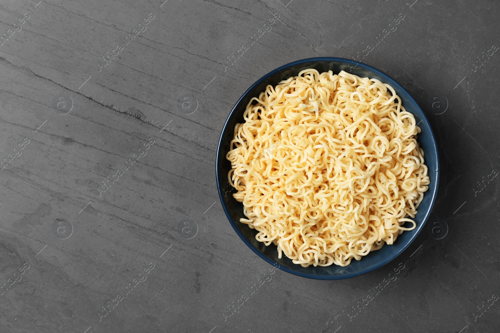 Photo of Bowl with tasty instant noodles on table, top view. Space for text