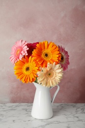 Bouquet of beautiful bright gerbera flowers in vase on marble table against color background