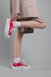 Photo of Woman putting on red classic old school sneakers against light gray background, closeup