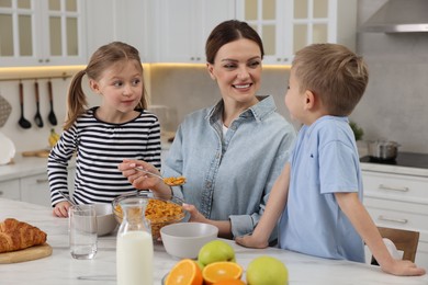 Mother and her little children having breakfast at table in kitchen