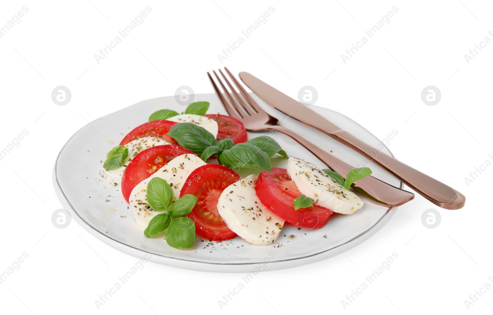 Photo of Plate of delicious Caprese salad with tomatoes, mozzarella, basil, spices and cutlery isolated on white