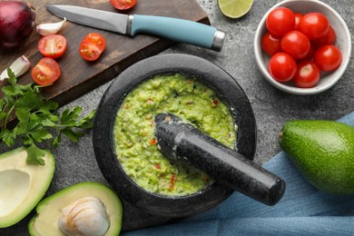 Photo of Mortar with delicious guacamole and ingredients on grey table, flat lay