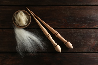 Soft wool and spindles on white wooden table, flat lay