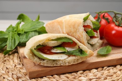 Photo of Delicious pita sandwiches with mozzarella, tomatoes and basil on wicker mat