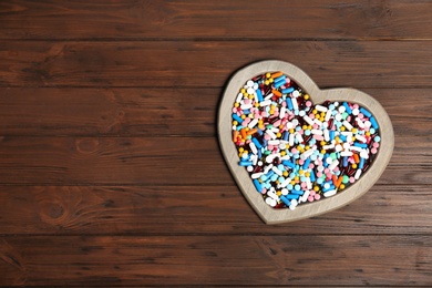 Photo of Heart shaped plate with different pills on wooden background. Cardiology concept