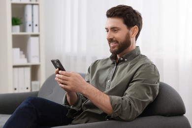 Smiling man using smartphone on sofa at home