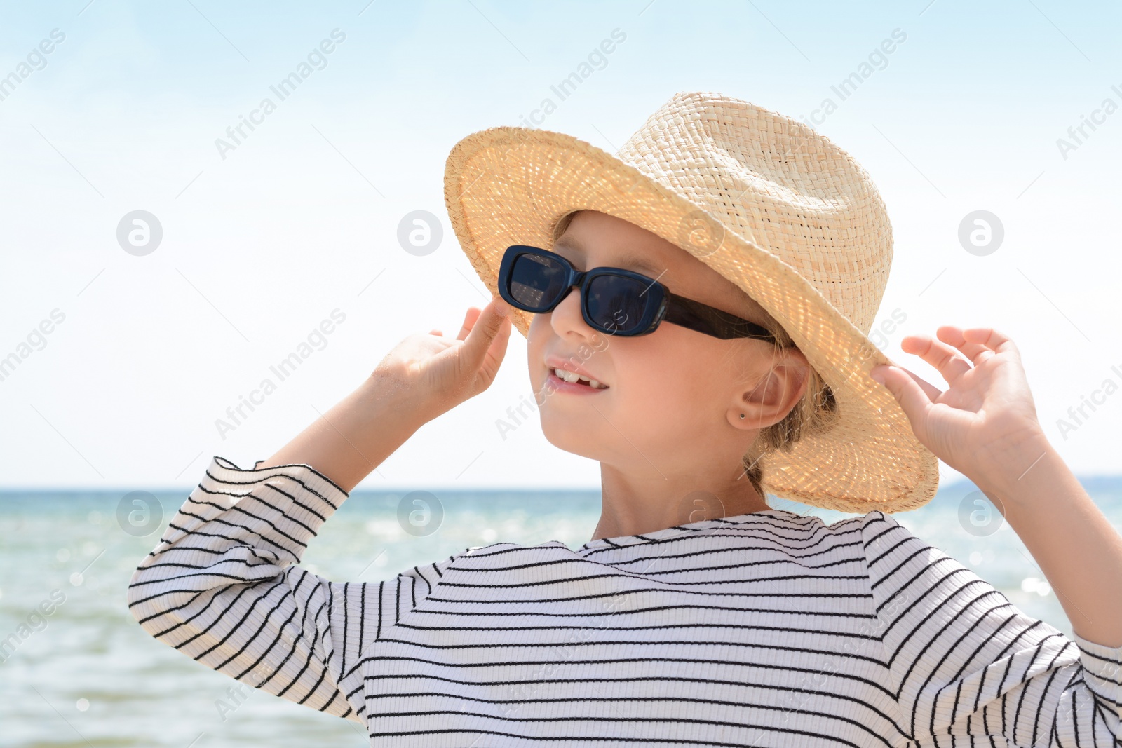 Photo of Little girl wearing sunglasses and hat at beach on sunny day