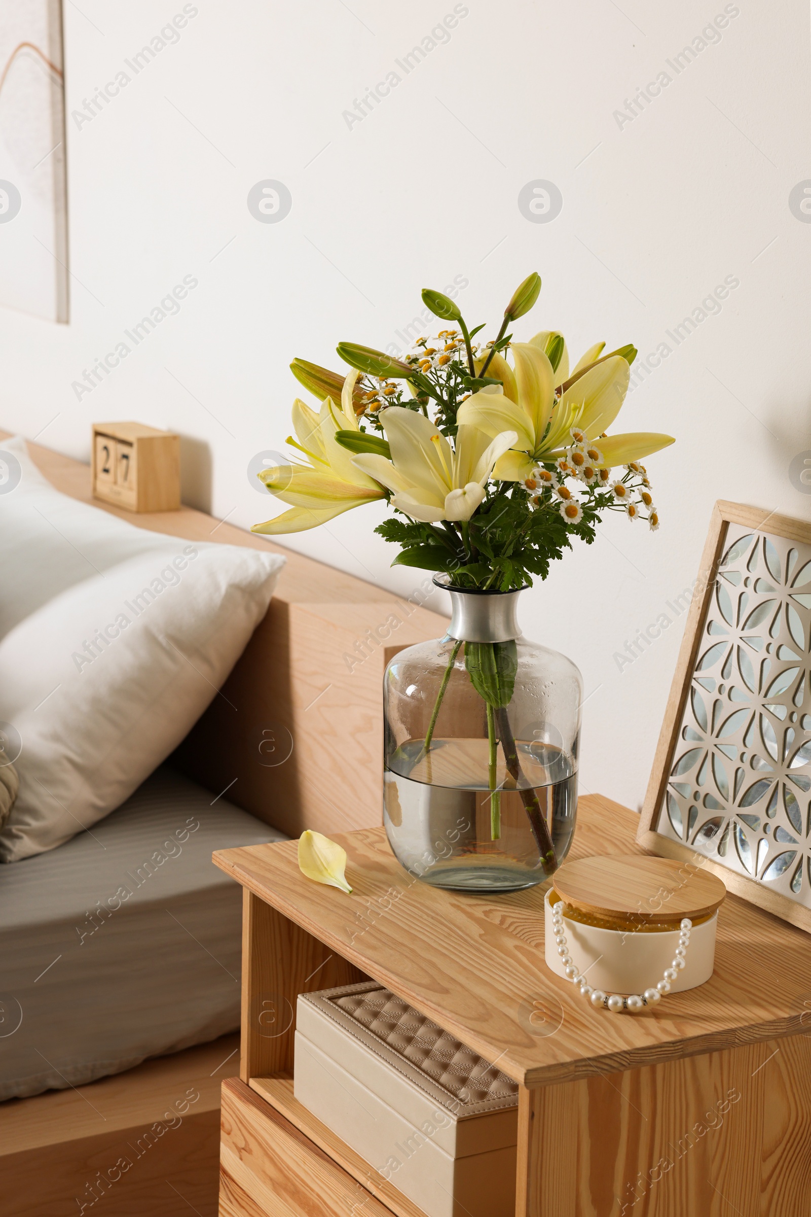 Photo of Vase with bouquet of fresh flowers on wooden nightstand in bedroom