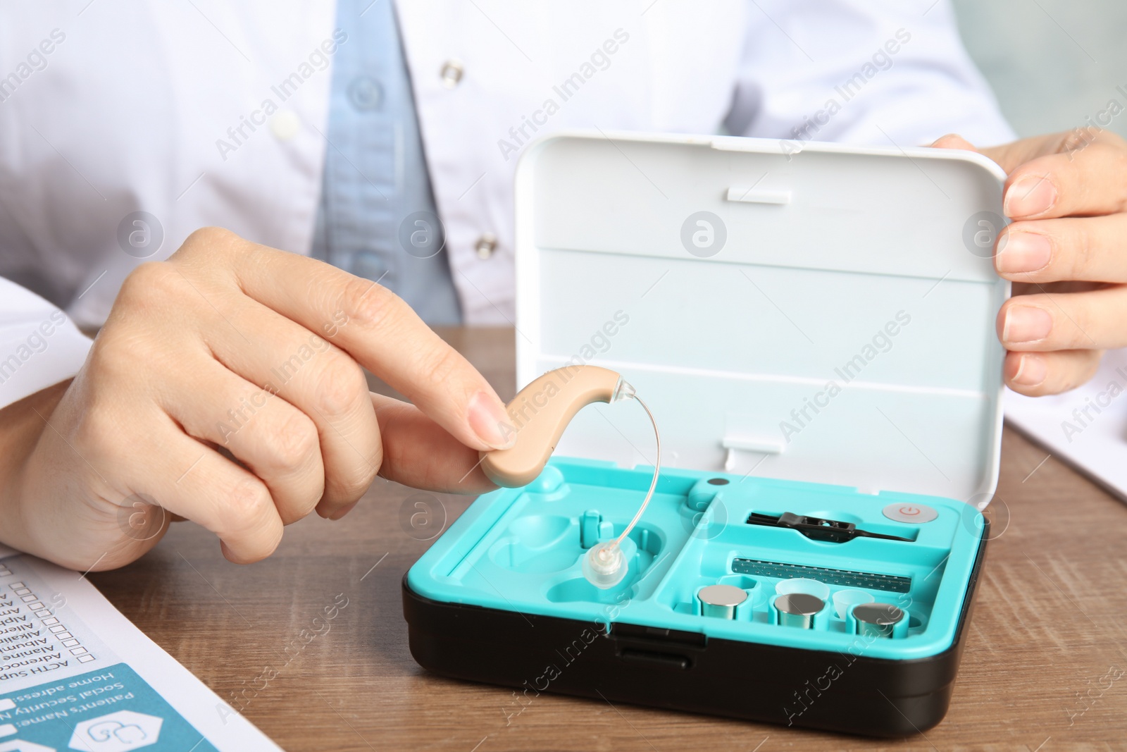 Photo of Doctor putting hearing aid into box at table, closeup. Medical device