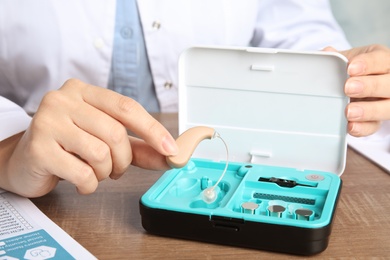 Photo of Doctor putting hearing aid into box at table, closeup. Medical device