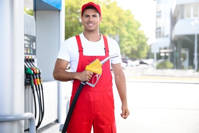 Worker with fuel pump nozzle at modern gas station